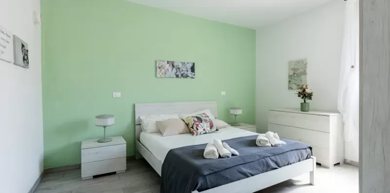 Un dormitorio con una cama frente a una pared verde pálido y mesitas de noche.