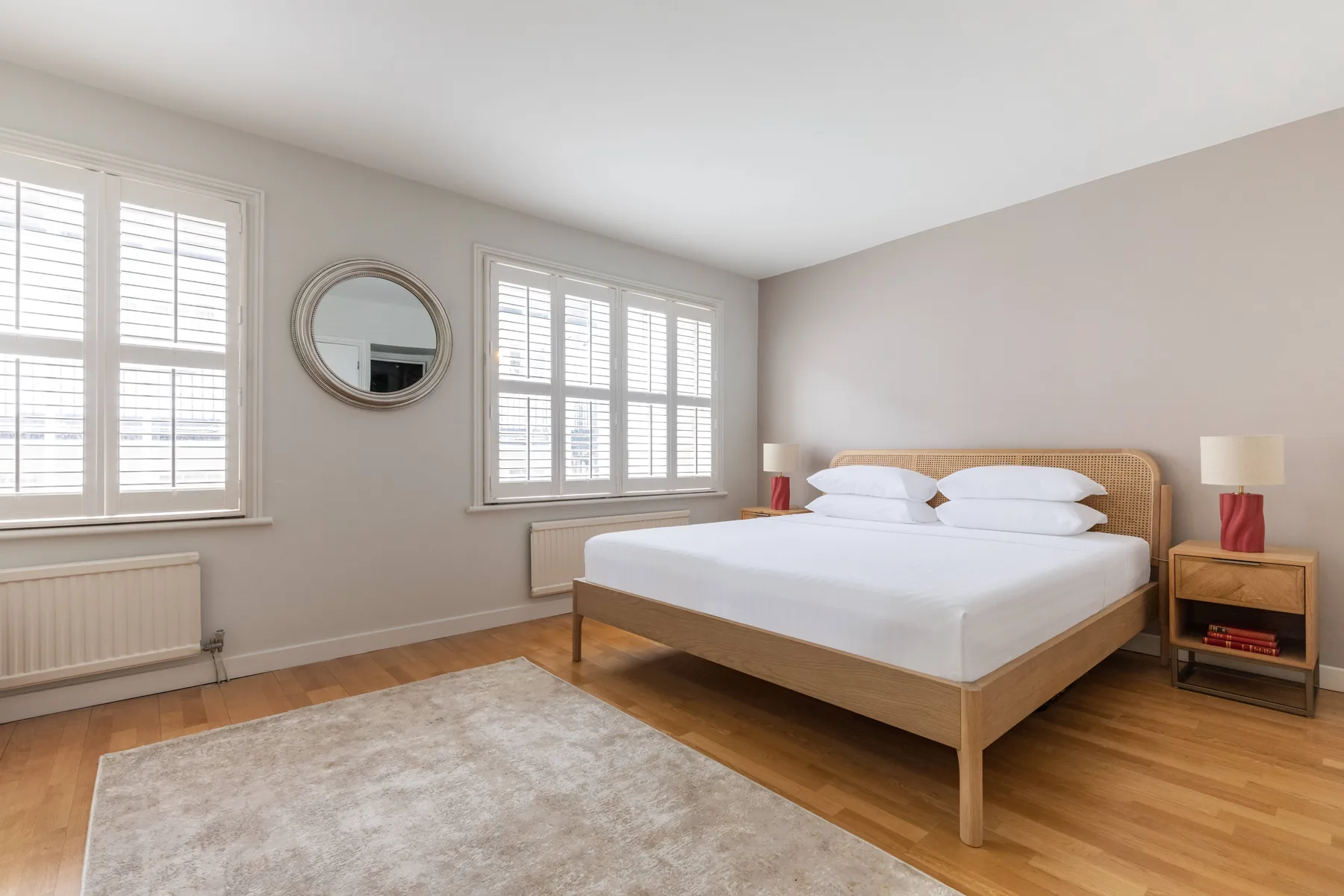 A bright bedroom with a neatly made bed, large windows, and a light rug.