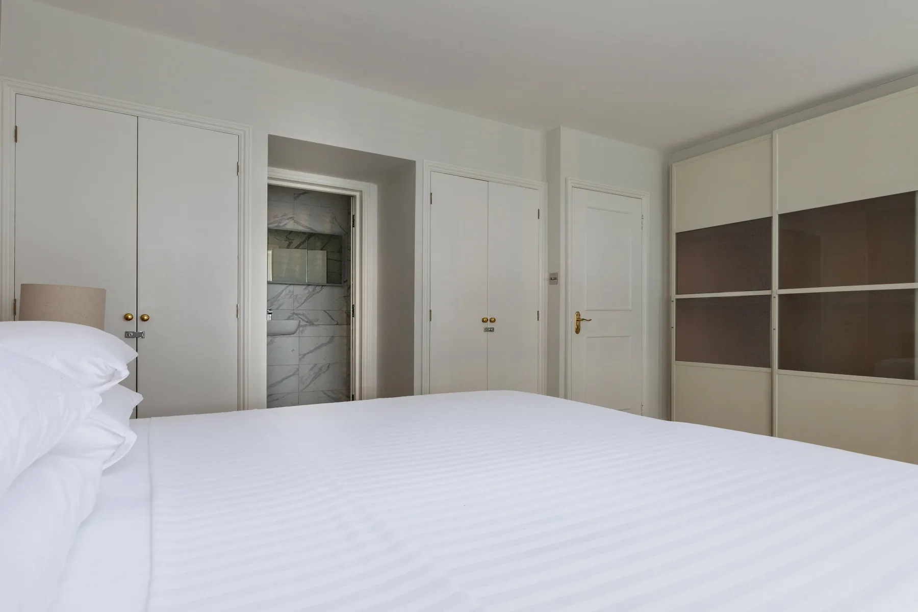 A bright bedroom with white bedding and built-in wardrobes.