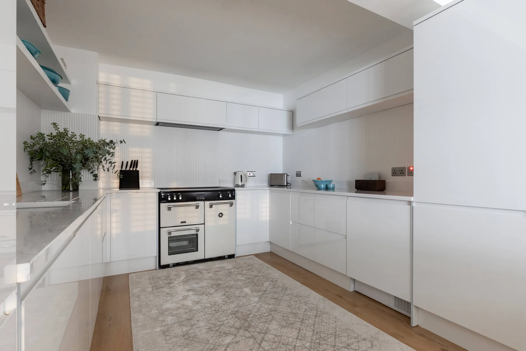 A bright white kitchen with built-in appliances and a long central counter.