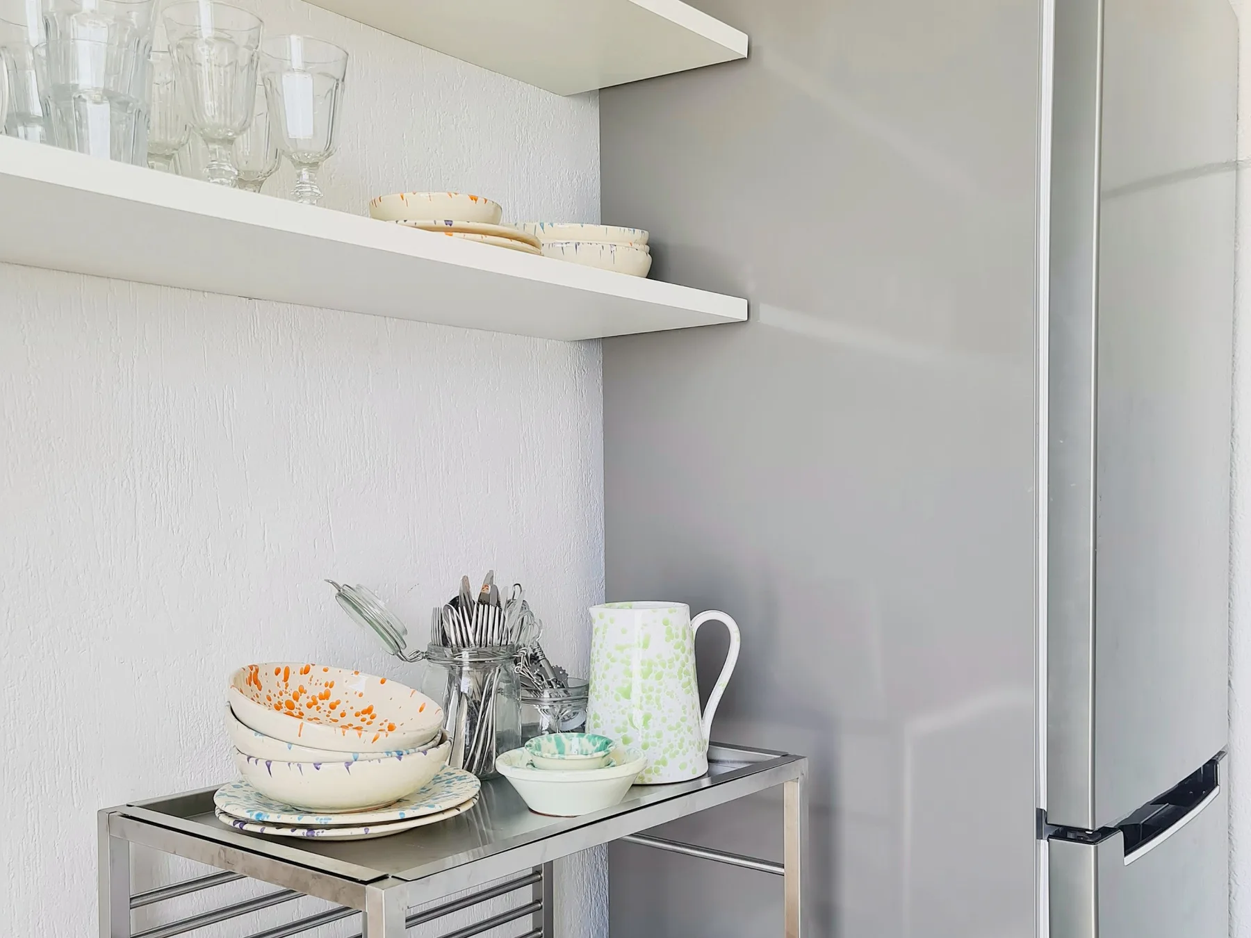 Una zona de almacenamiento de cocina con vajilla y cristalería en estantes junto a un refrigerador.