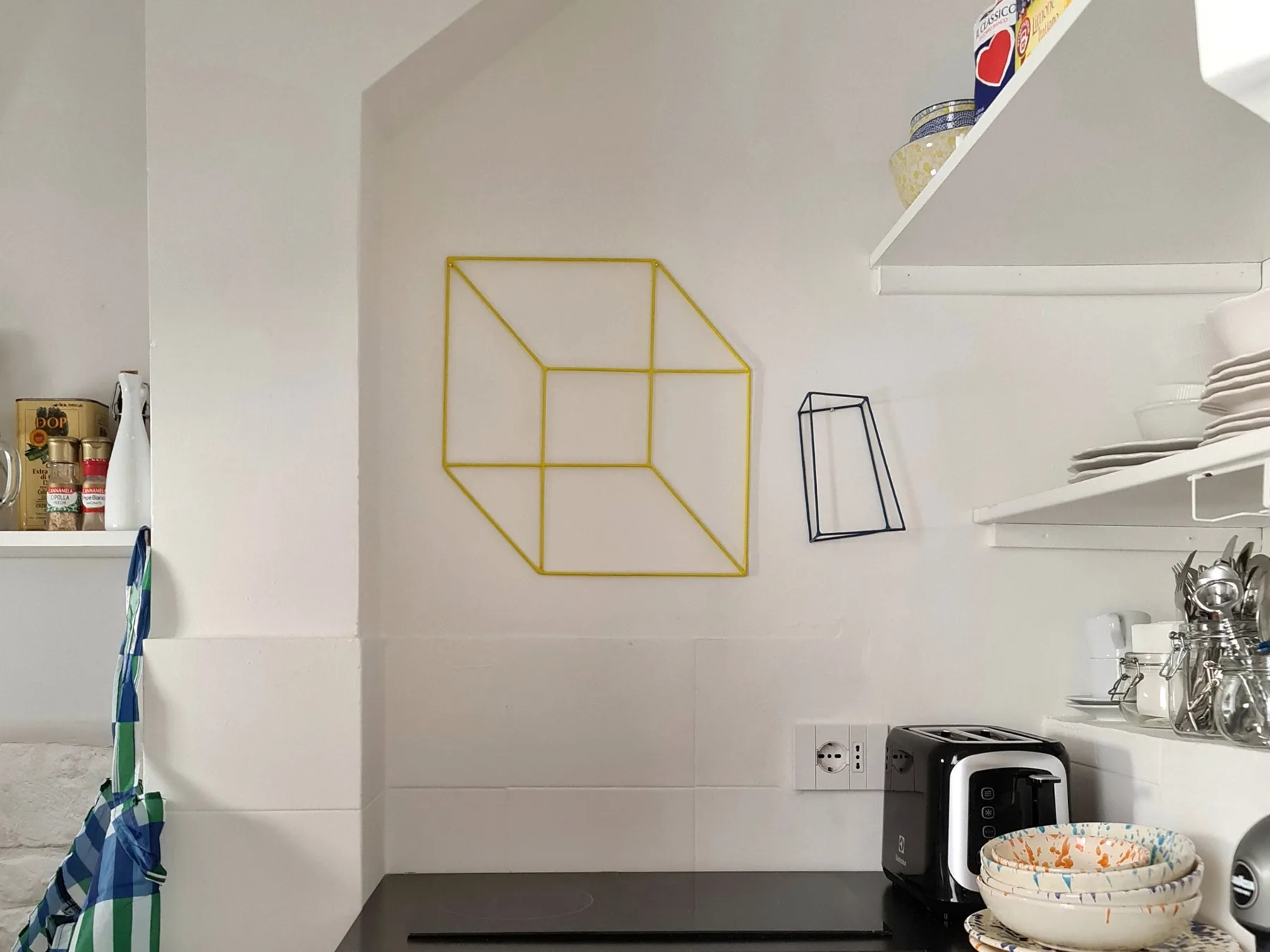 Una pequeña encimera de cocina con tostadora, platos y adornos geométricos en la pared.