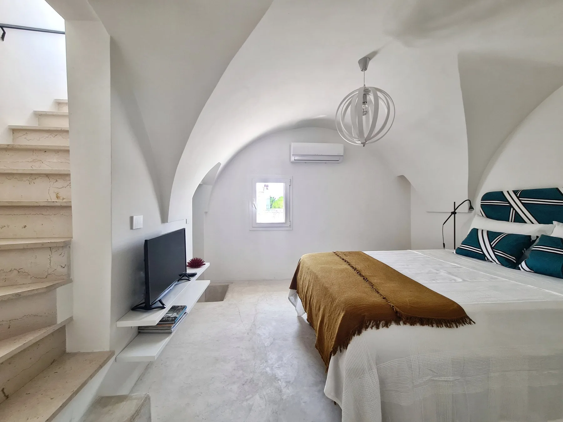 Un dormitorio con una cama, un televisor en la pared y una escalera.