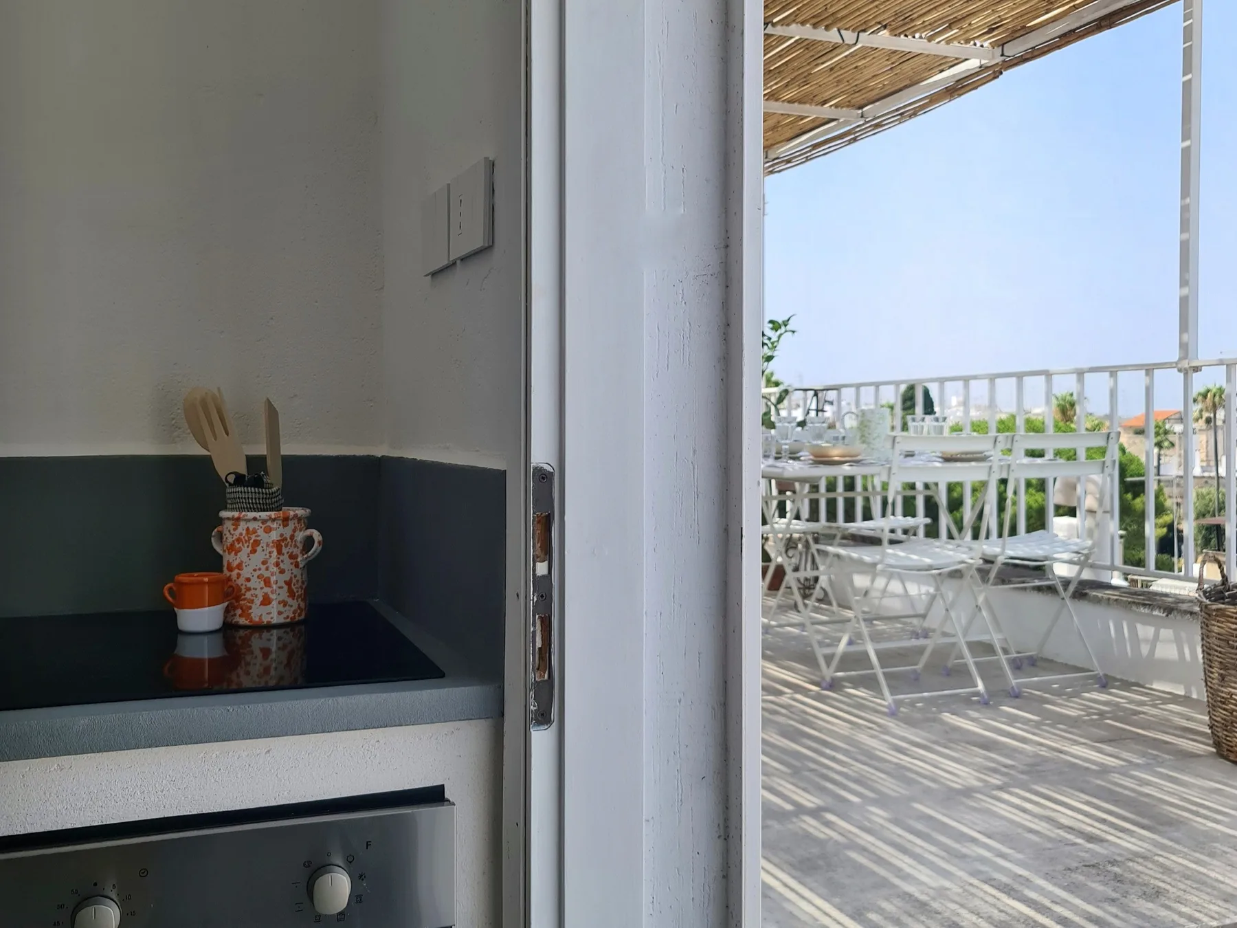 Una cocina se abre a una zona exterior para comer con mesas y asientos blancos.