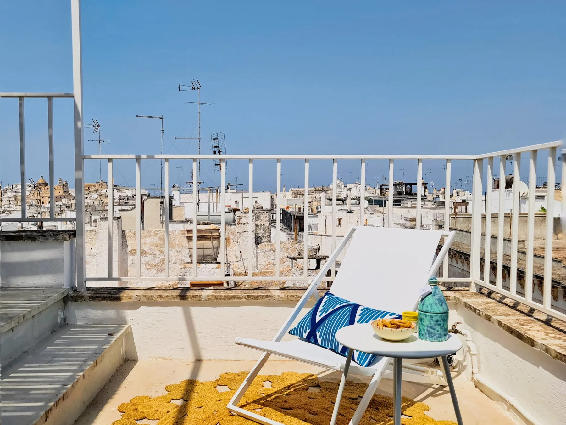 Una terraza en la azotea tiene una silla reclinable, una mesa pequeña y vistas a edificios cercanos.