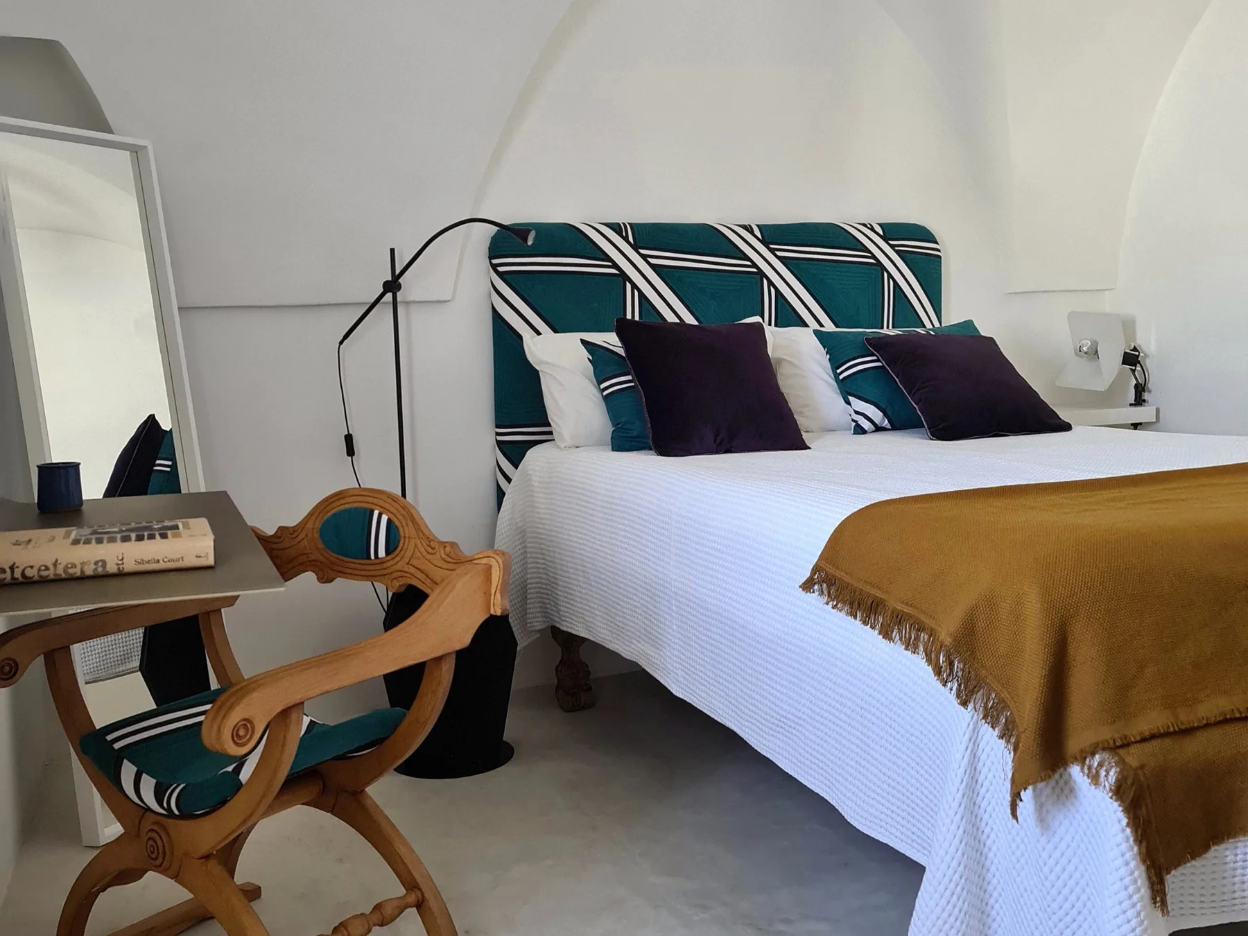 Un dormitorio con una cama vestida de blanco y un cabecero estampado en tonos verdes.