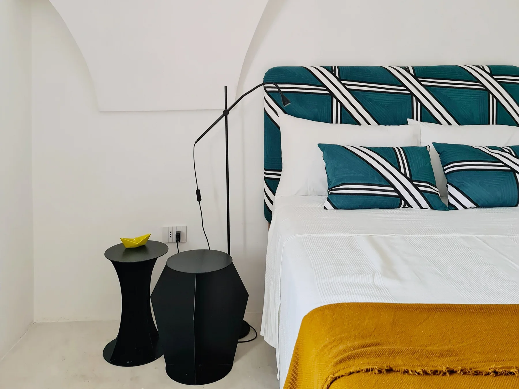 Un dormitorio con una cama blanca, almohadas a rayas turquesas y una manta color mostaza.