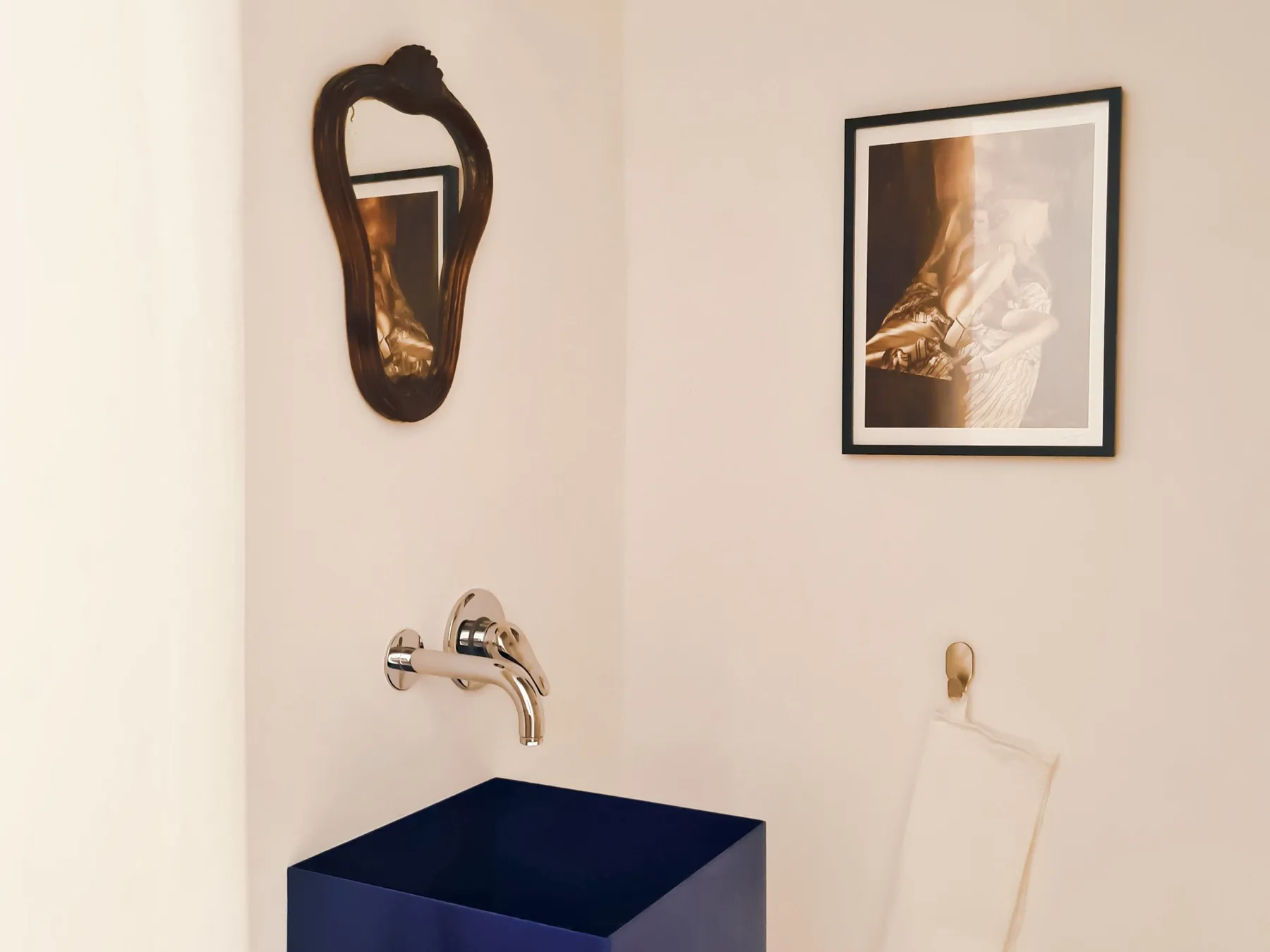 Un lavabo de baño bajo un espejo de pared, con una obra enmarcada cerca.