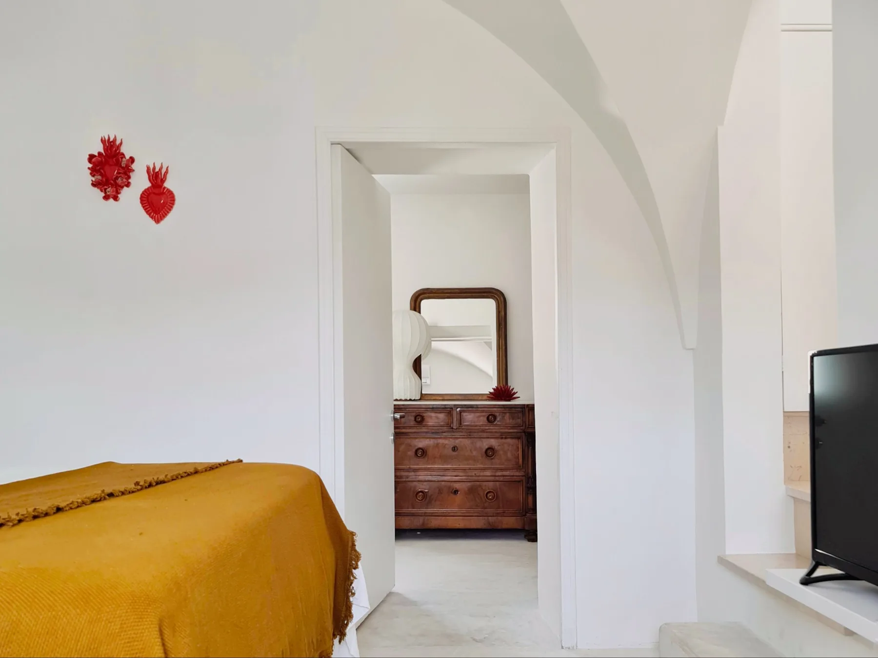 Un dormitorio con una colcha color mostaza y una cómoda visible a través de la puerta.