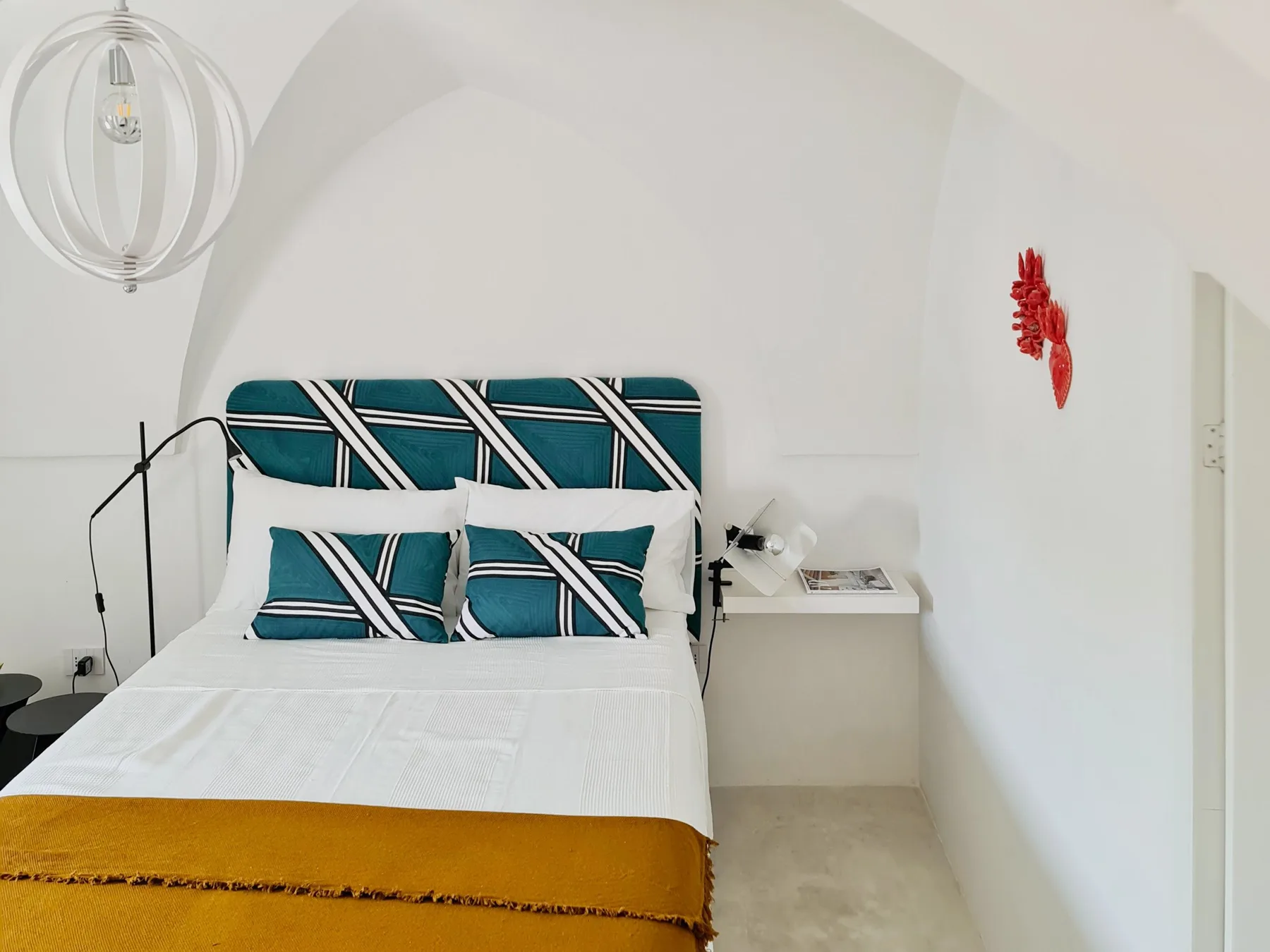 Un dormitorio con una cama vestida con ropa de cama estampada en tonos turquesa y una colcha mostaza.