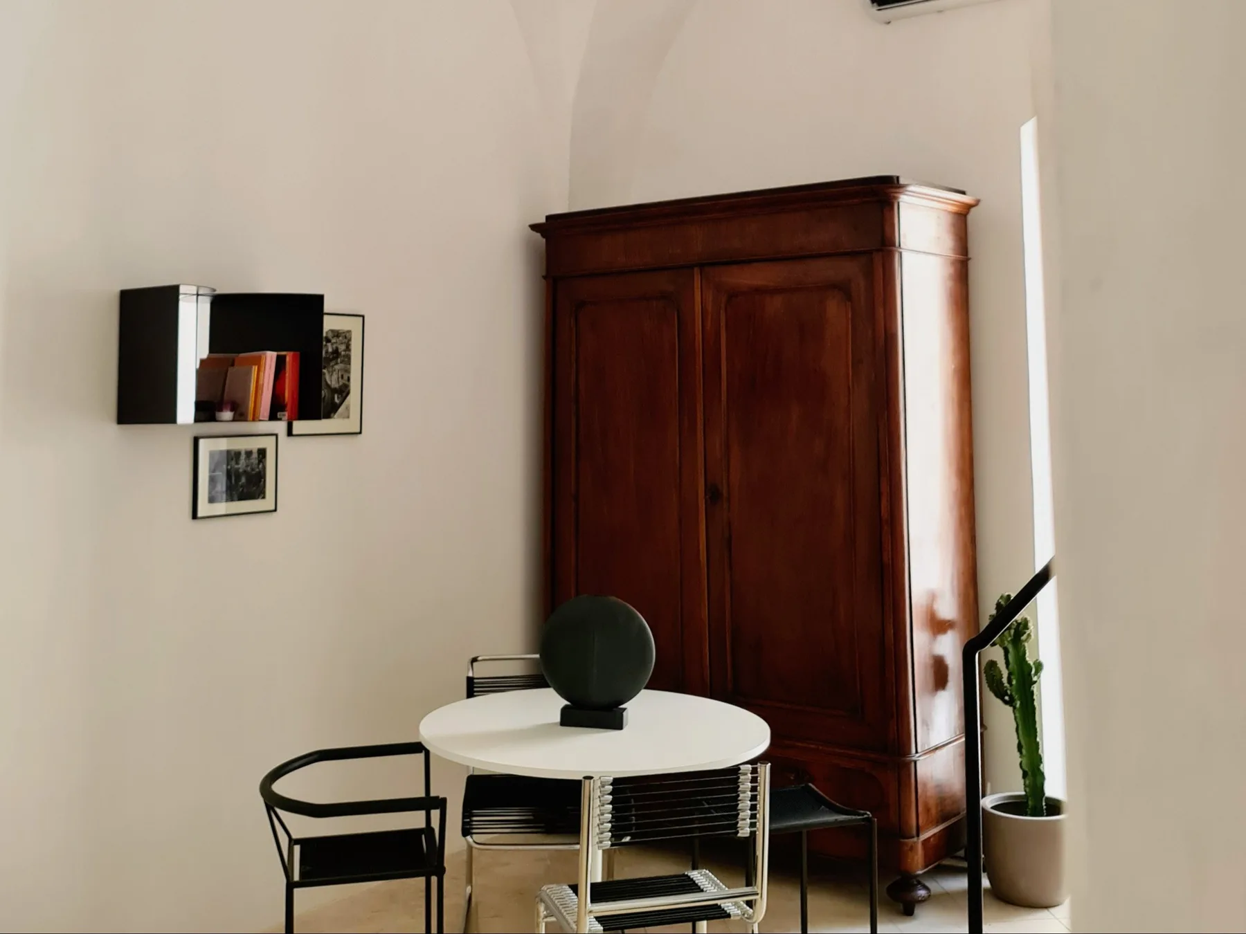 Una habitación luminosa con una mesa redonda, asientos y un armario alto de madera.