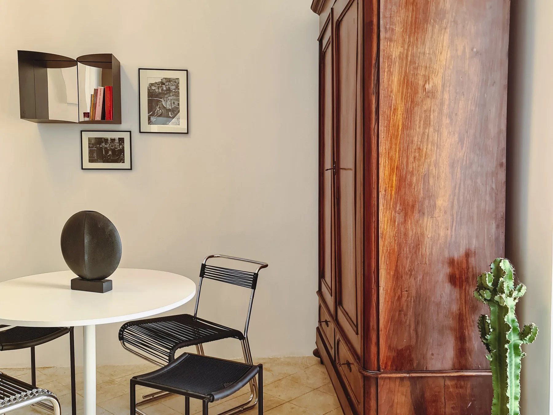 Una pequeña zona de comedor tiene una mesa redonda, asientos oscuros y cuadros en la pared.