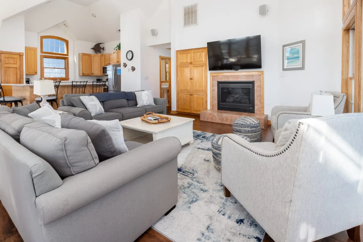 A bright living room with gray seating arranged around a coffee table and fireplace.