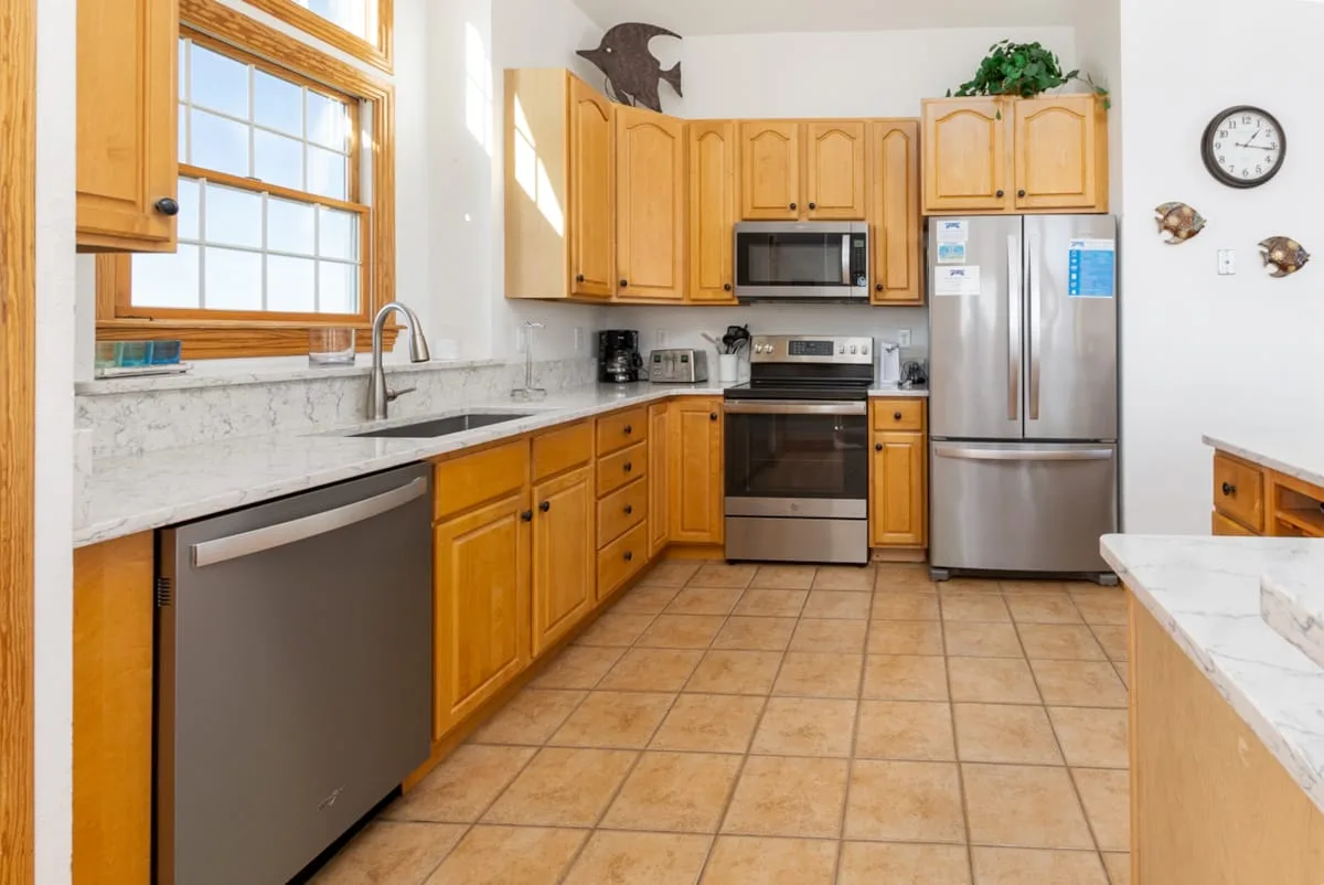 A bright kitchen with wooden cabinets, stainless steel appliances, and tiled flooring.