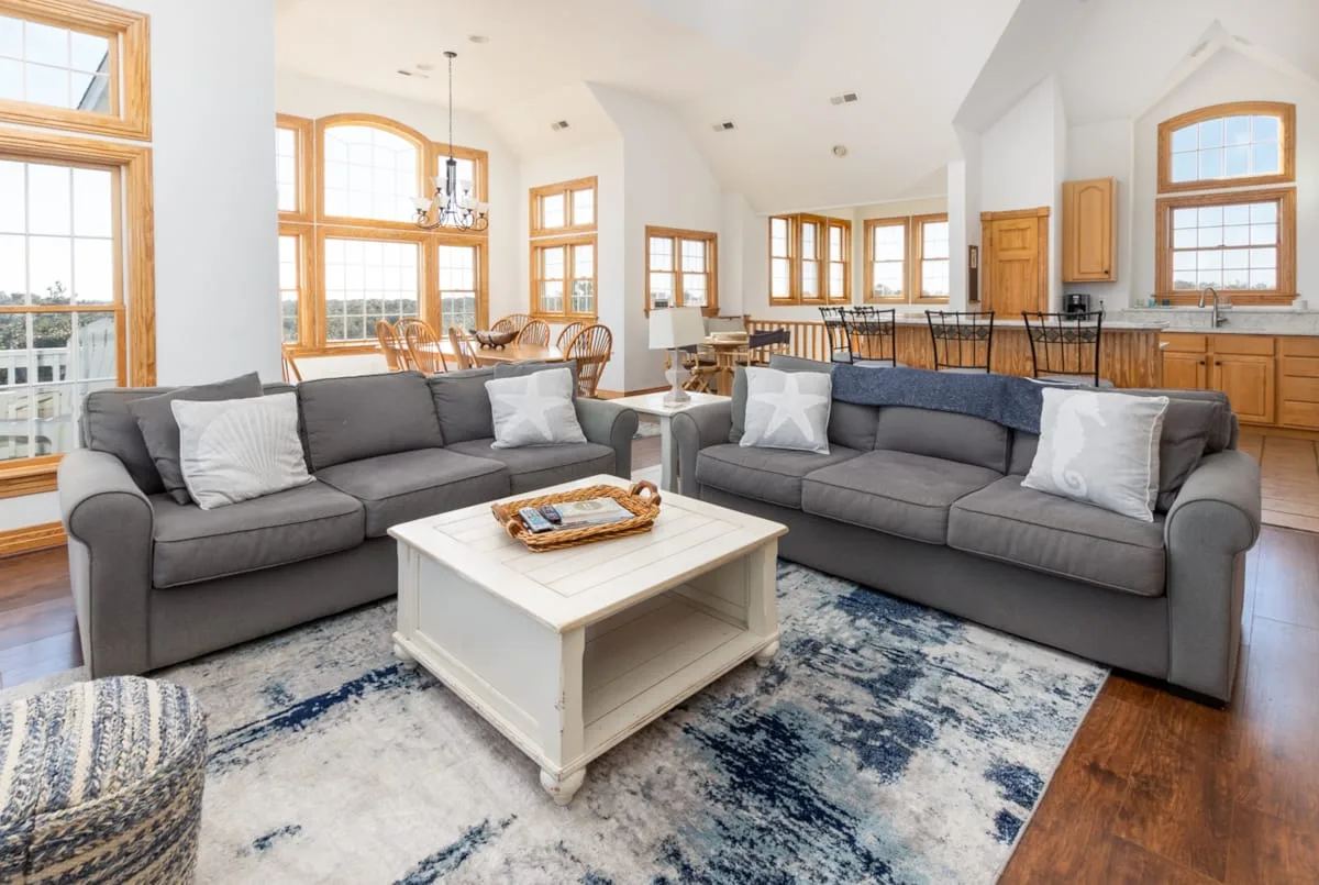 A bright living room with gray seating, a white coffee table, and large windows.