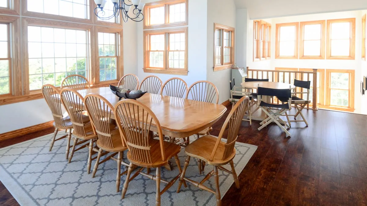 A bright dining room with a long wooden table and large windows.
