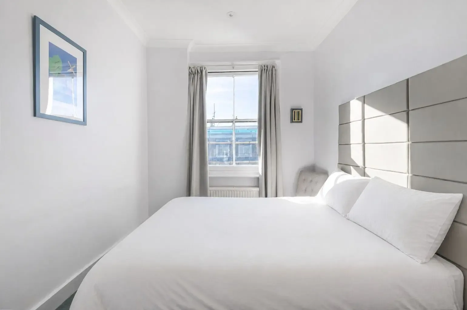 A bedroom with a neatly made bed and a window with curtains.