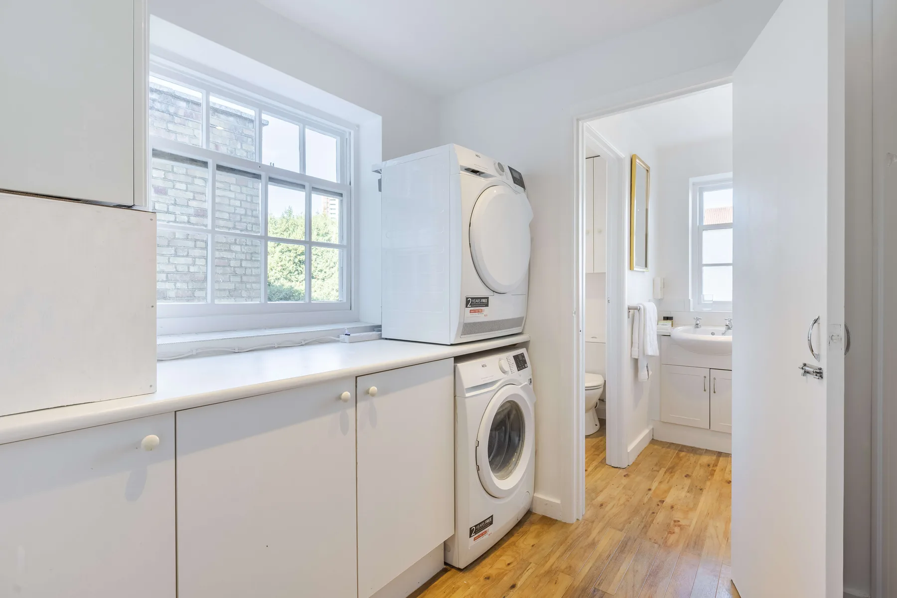 A bright laundry room with stacked washer and dryer beside a large window.