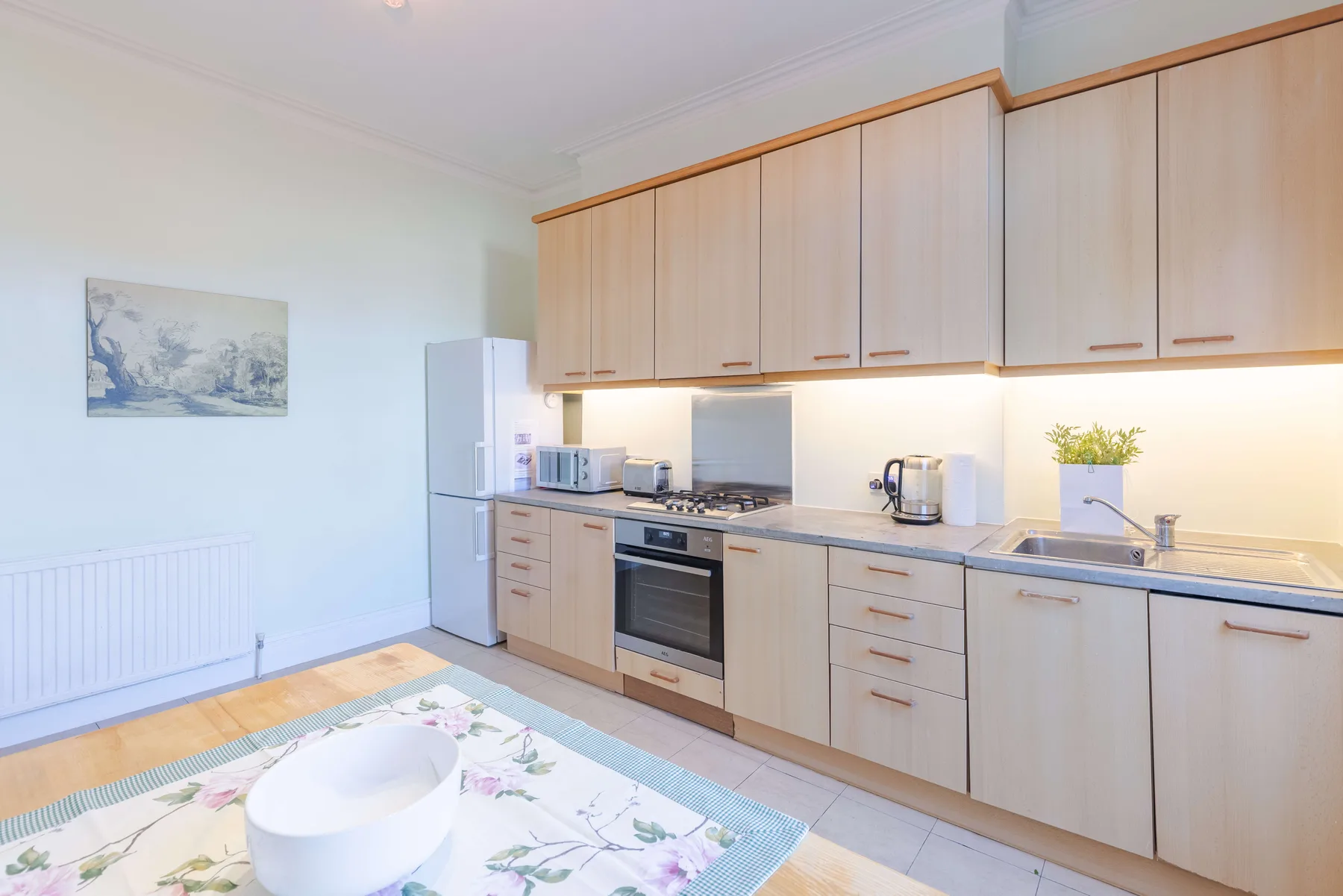 A bright kitchen with pale cabinets and a dining table in the foreground.