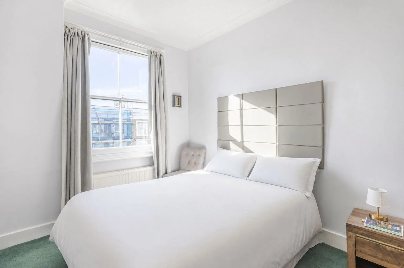A bright bedroom with a large bed beside a curtained window.