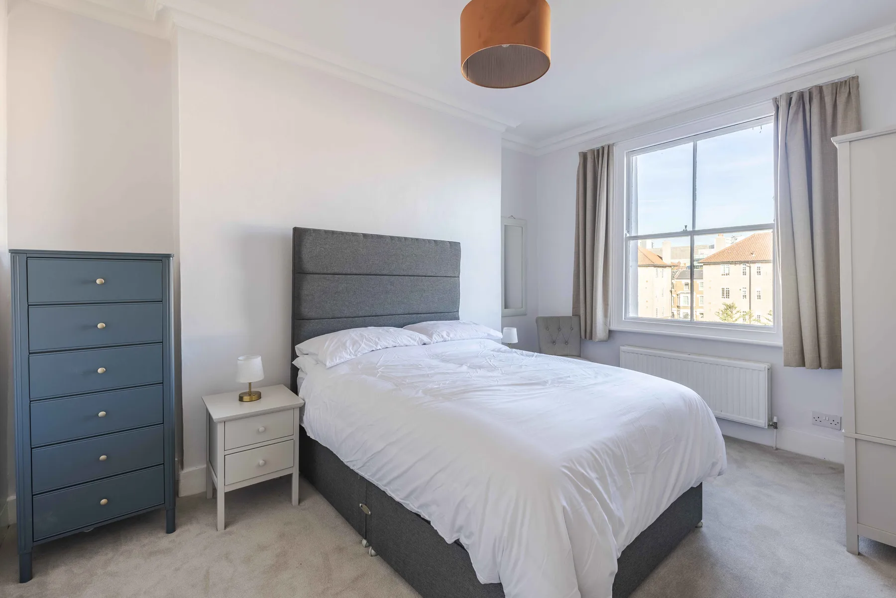 A bright bedroom with a neatly made bed beside a large window.