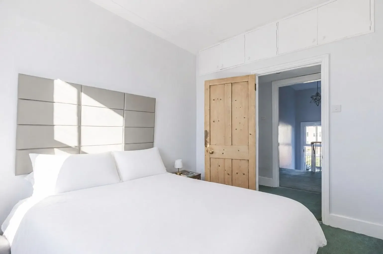 A bright bedroom with a white bed and wooden door.