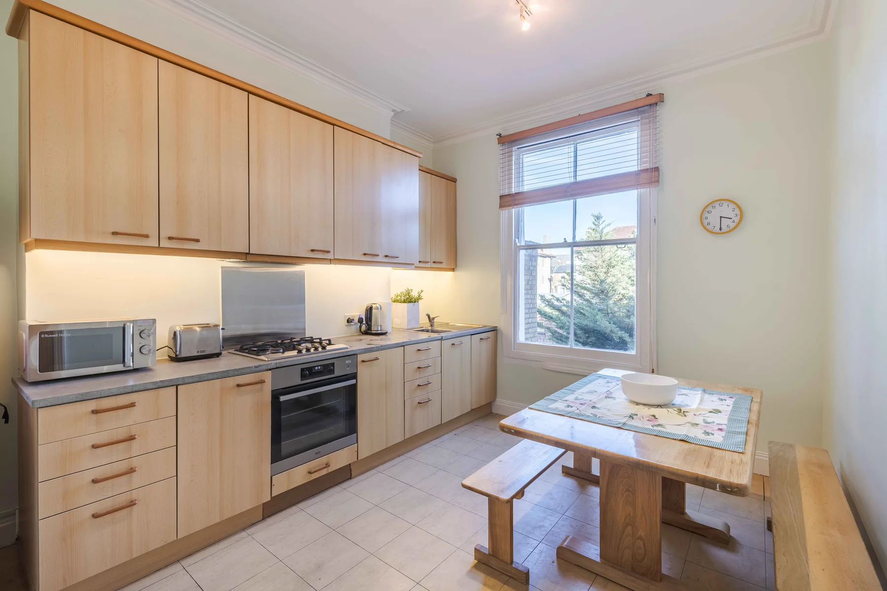 A bright kitchen with light wood cabinets, cooking appliances, and a dining table by the window.