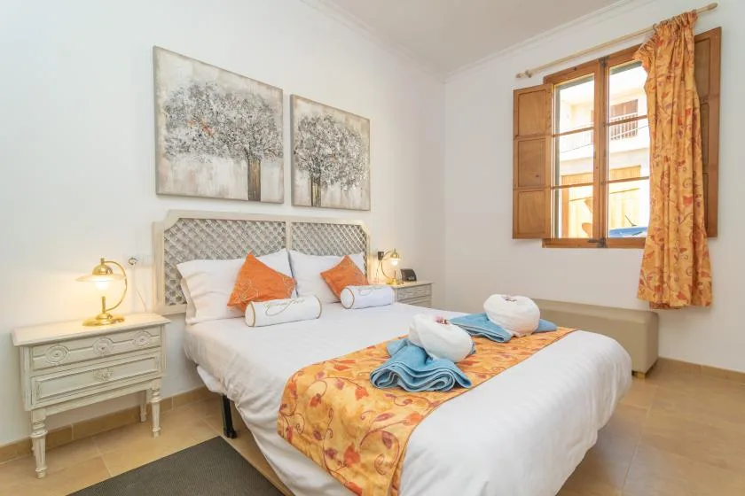 A bright bedroom with a double bed, patterned runner, and wooden-framed window.