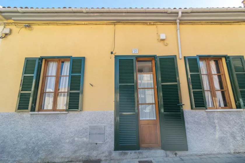 Yellow building facade with a central wooden door and shuttered windows.