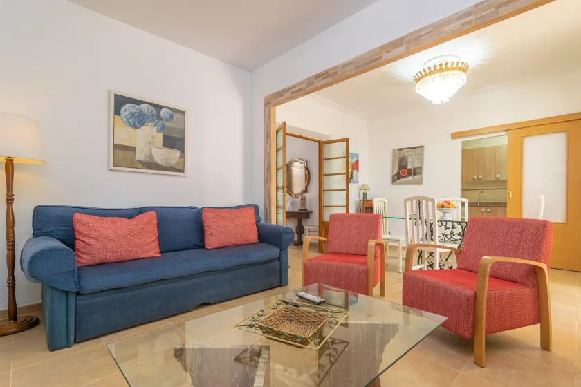 A living room with a blue sofa and red armchairs around a glass coffee table.