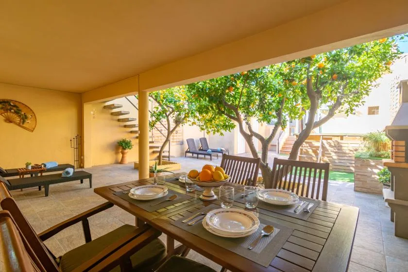 A covered outdoor dining area with a table, seating, and leafy trees beyond.
