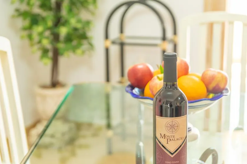 A dining area with a fruit bowl and wine bottle on a glass table.