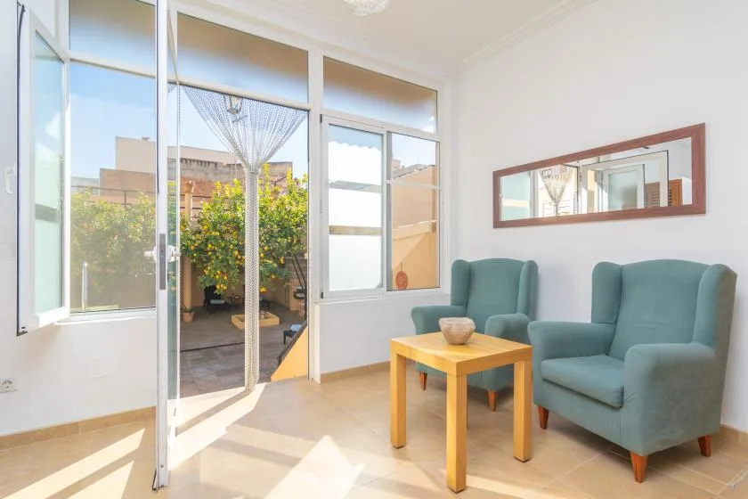 A bright sitting area with two upholstered seats and a wooden table beside large windows.