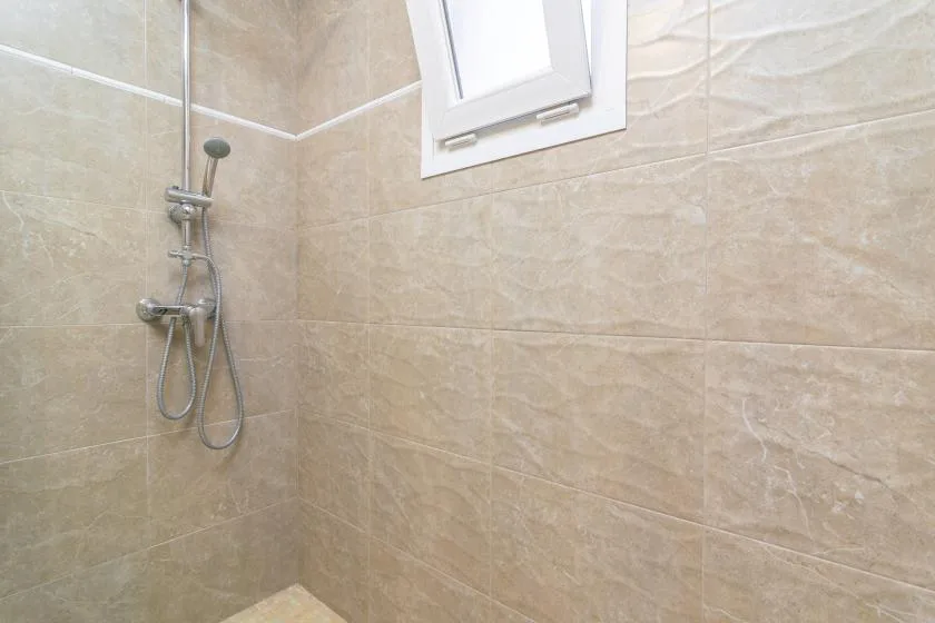 A tiled shower area with a wall-mounted shower fixture and small window.