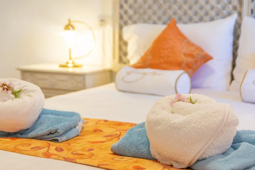 A neatly made bed features orange accents and folded towels arranged on top.