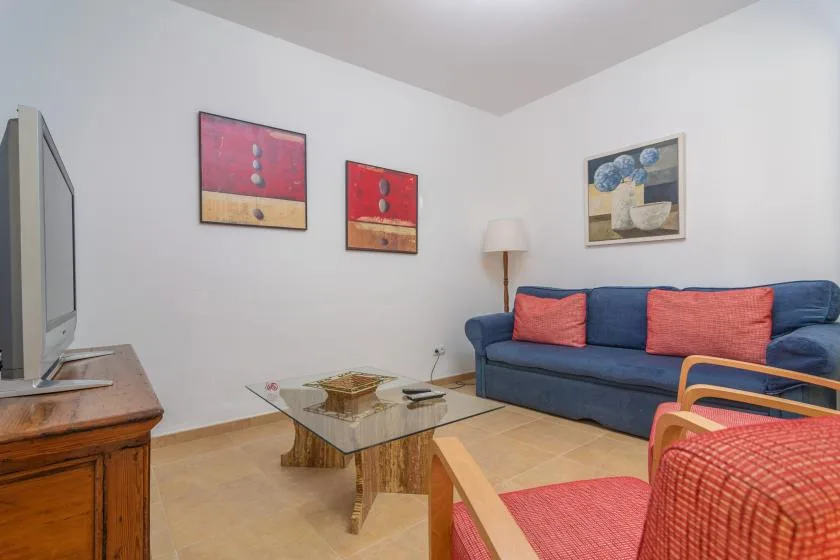 A living room with blue seating, a glass coffee table, and framed wall art.