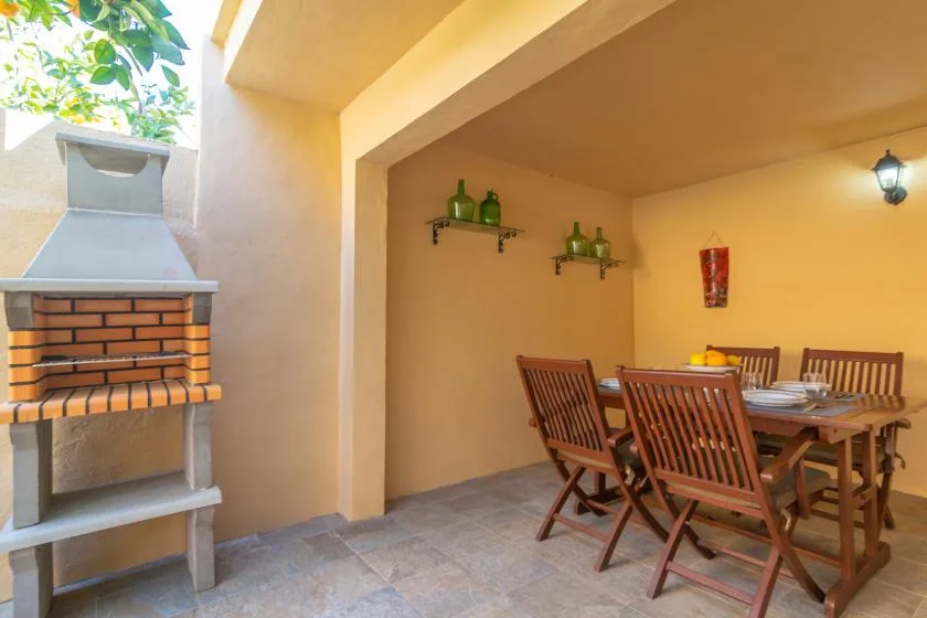 A covered outdoor dining area with a wooden table and a brick barbecue.