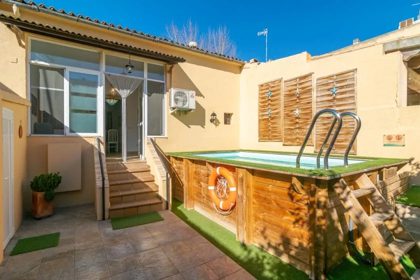 A sunny courtyard with a small raised pool beside a house entrance.