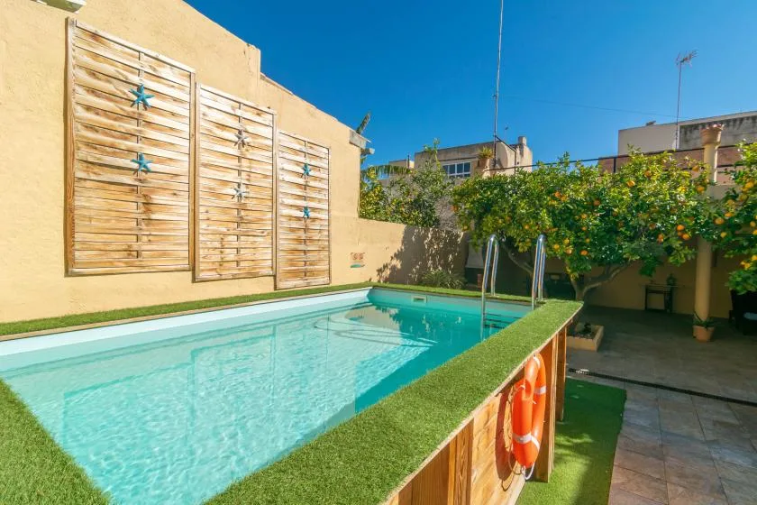 A small outdoor swimming pool sits beside a shaded patio with leafy plants.