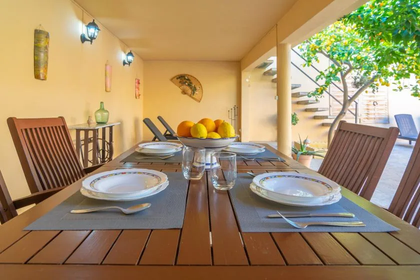 A covered outdoor dining area with a set table and a view of the garden.
