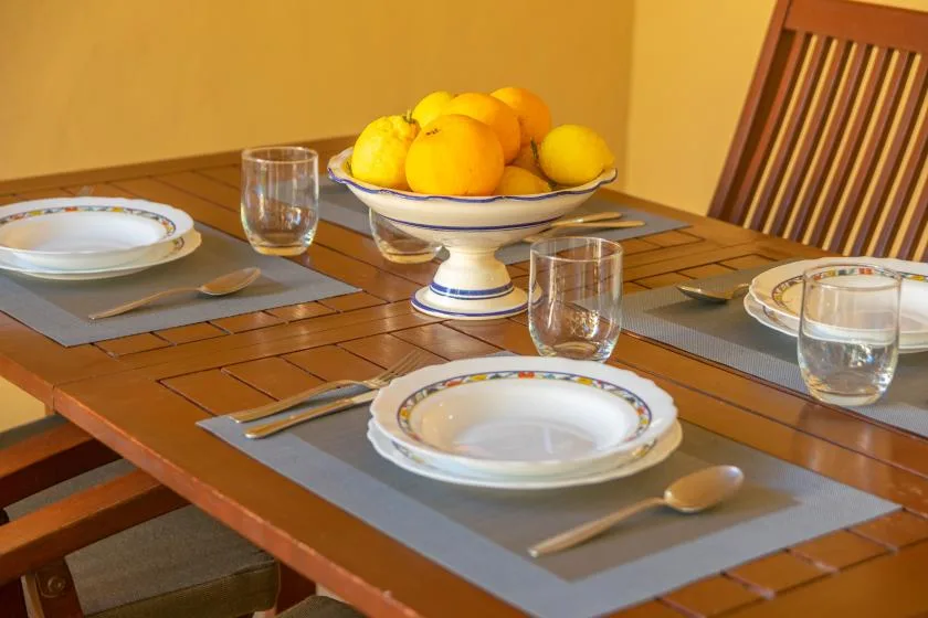 Dining area with a wooden table set with plates and a bowl of citrus fruit.