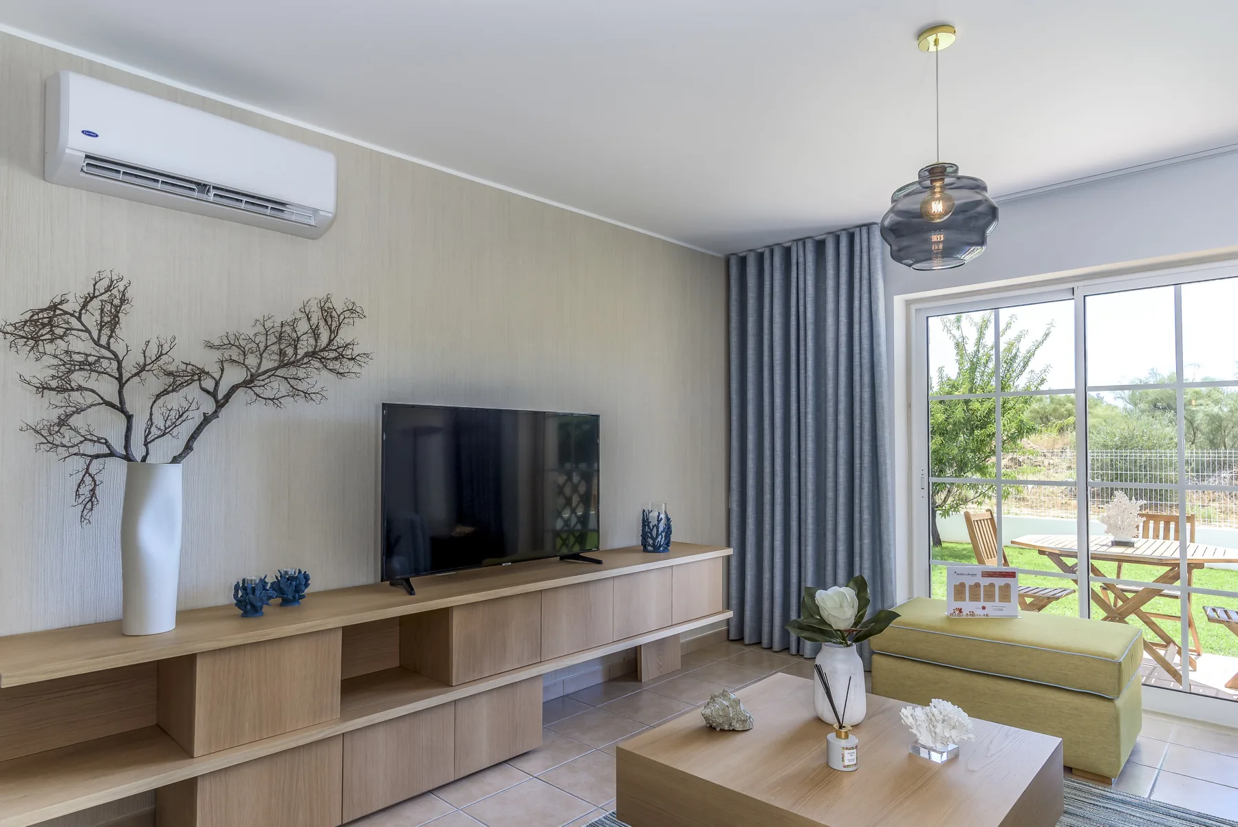 Una sala de estar con televisión, muebles bajos de madera y una puerta corredera de cristal.
