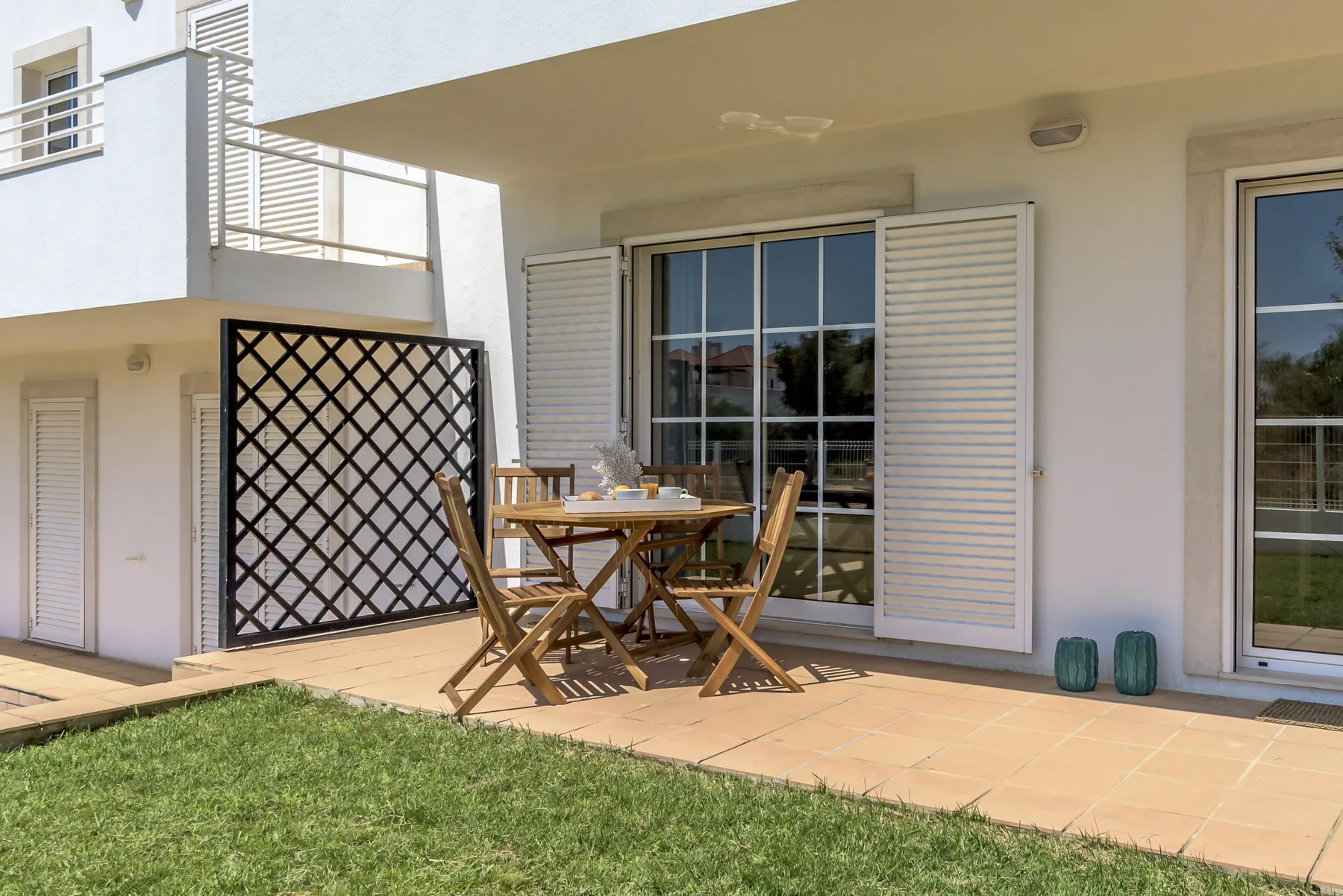 Un patio cubierto tiene una mesa de comedor de madera y sillas junto a puertas corredizas de vidrio.