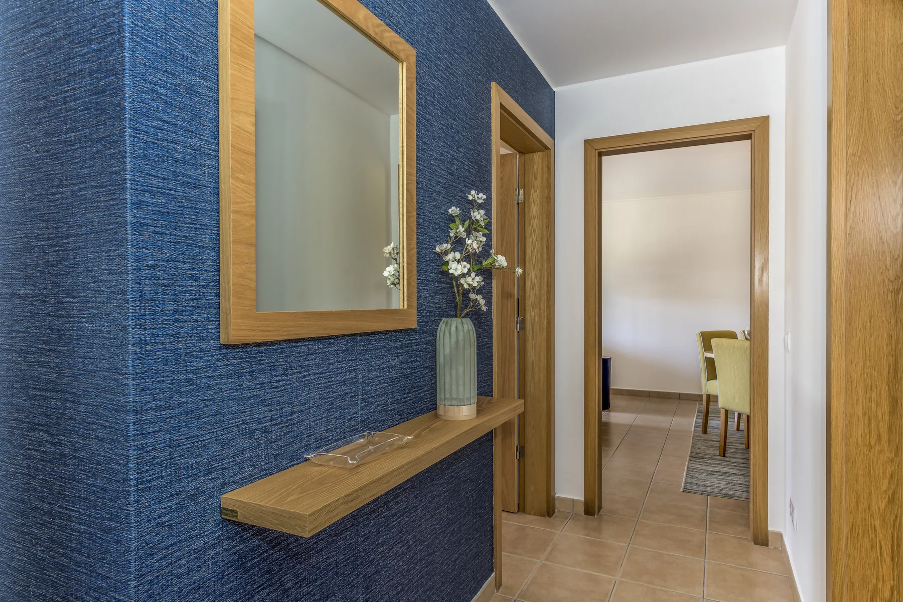 Un pasillo con un espejo y una pequeña consola junto a una pared azul texturizada.