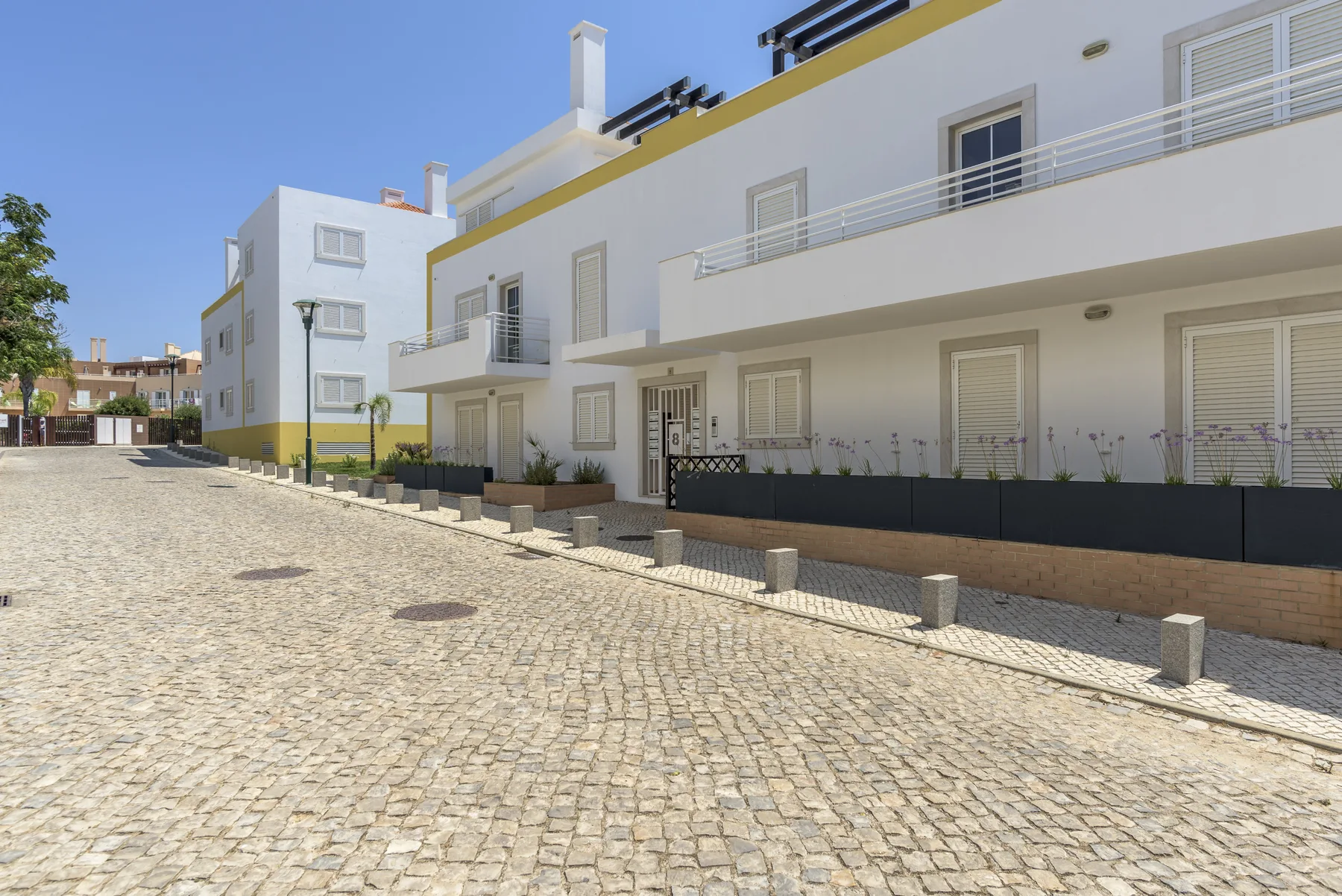Un edificio de apartamentos blanco con balcones junto a una calle adoquinada.