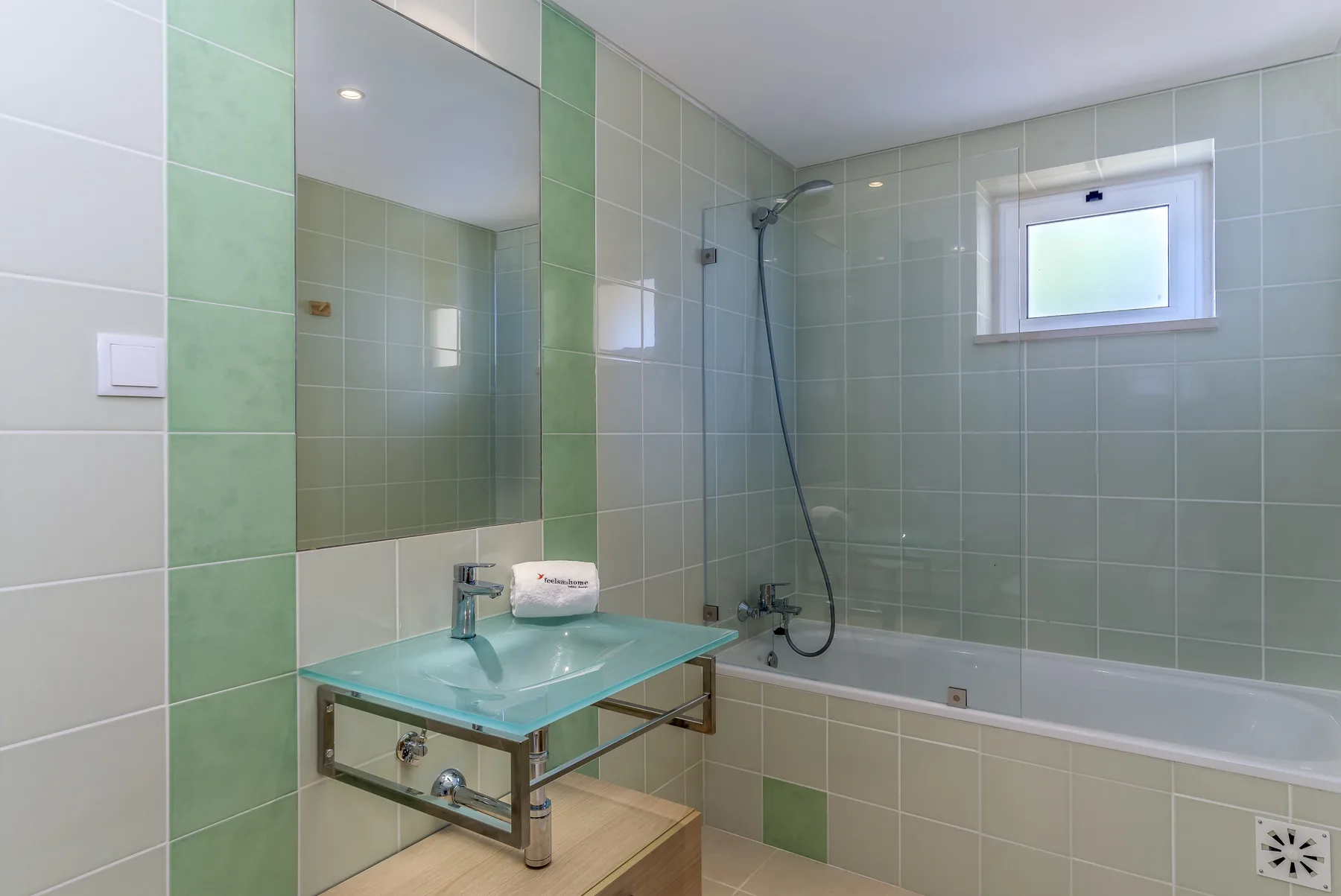 Baño alicatado con lavabo de vidrio y bañera.