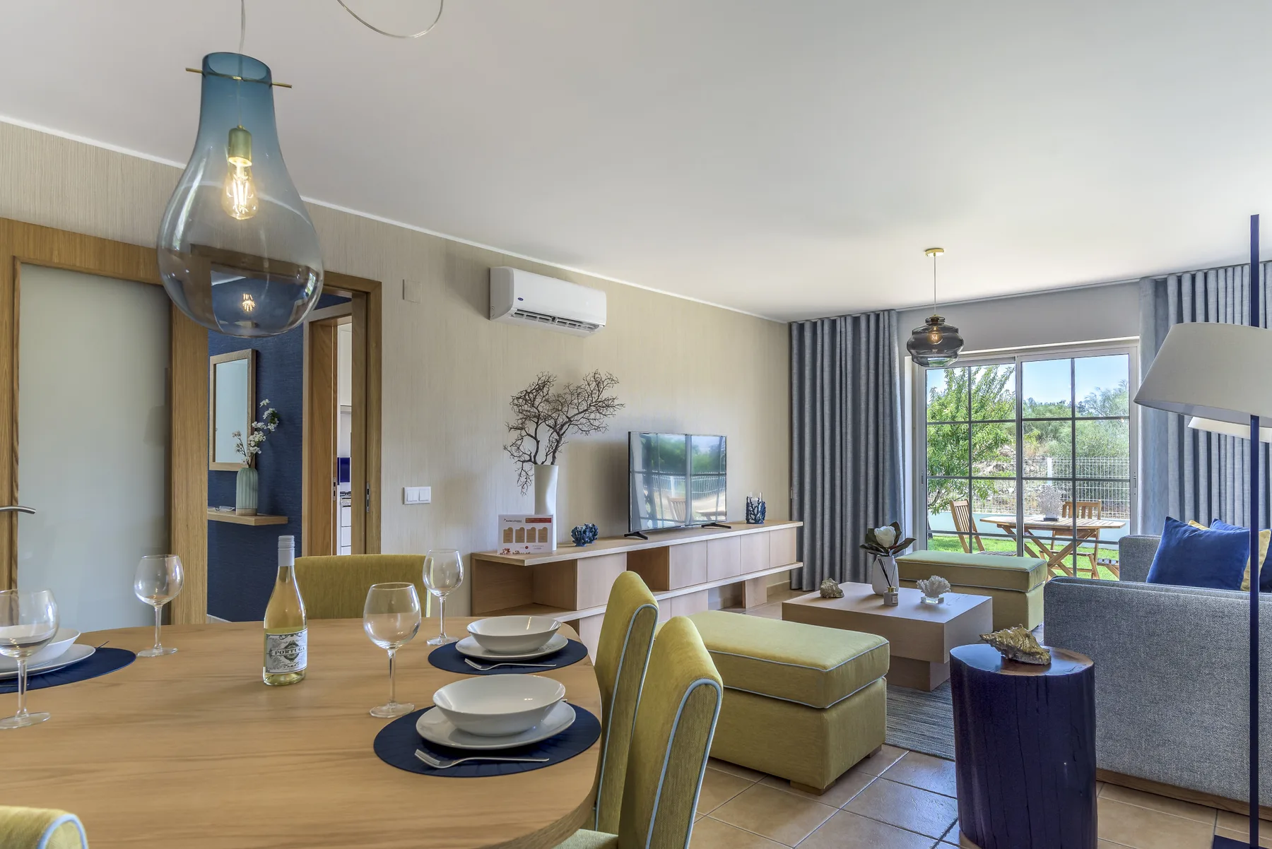 Una luminosa sala de estar y comedor con asientos, un televisor y puertas de vidrio que dan a un patio.