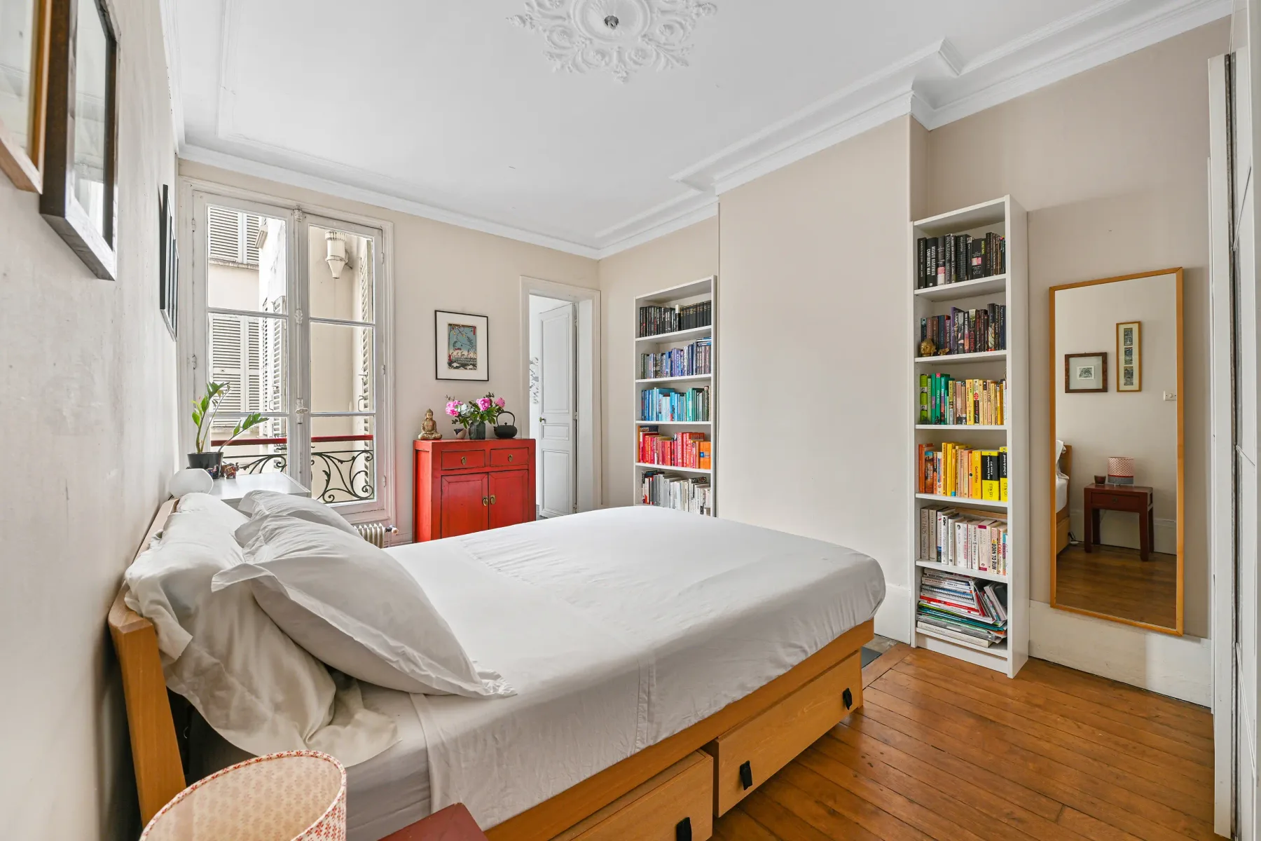 Un dormitorio luminoso con una cama, estanterías y un espejo alto.