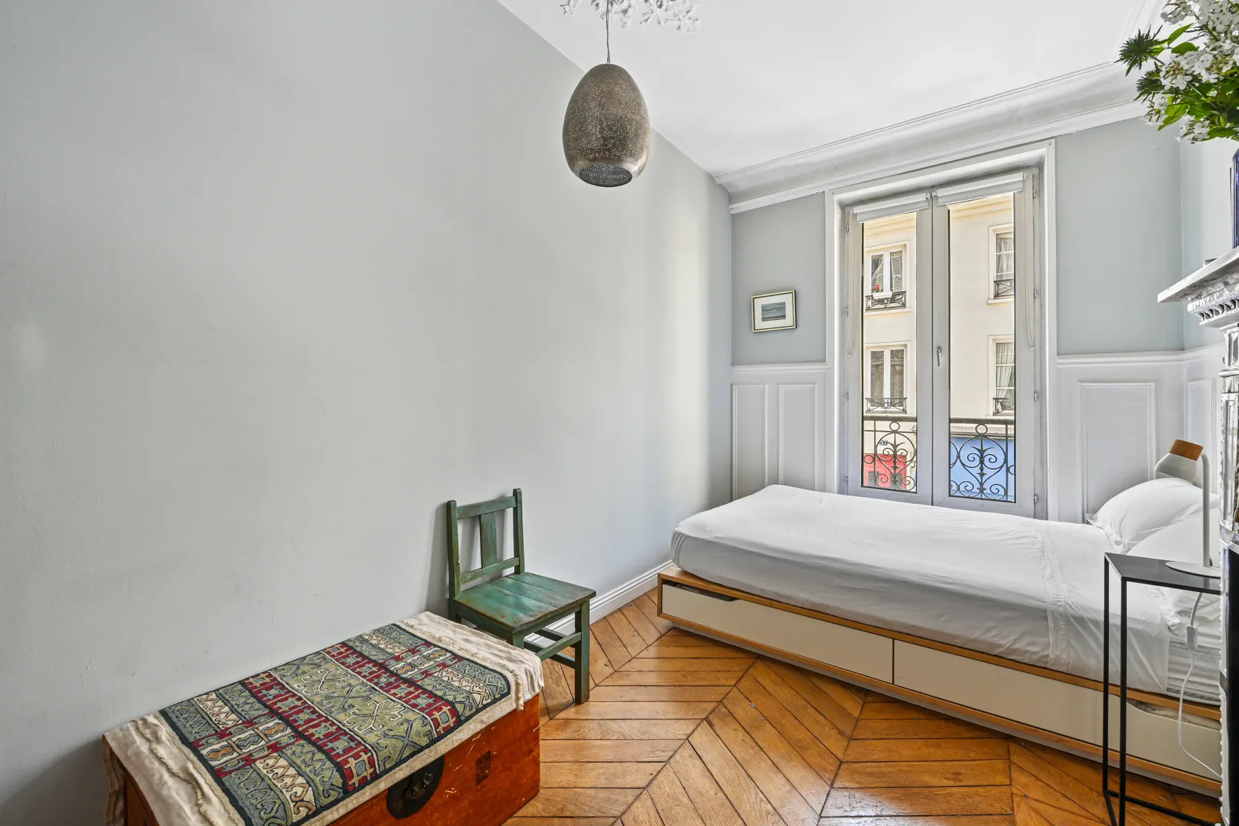 Un dormitorio luminoso con una cama, una silla verde y ventanas altas.