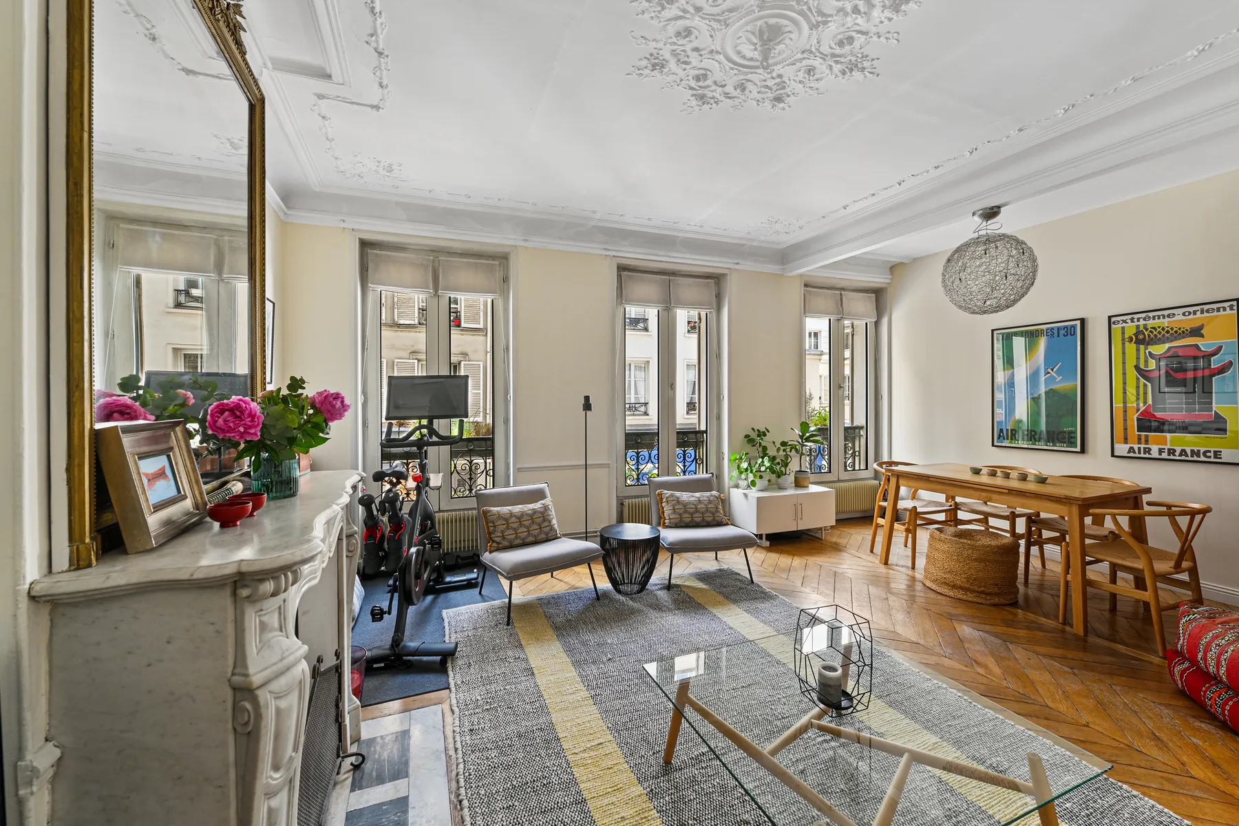 A bright living and dining room with tall windows, seating, and a wooden table.
